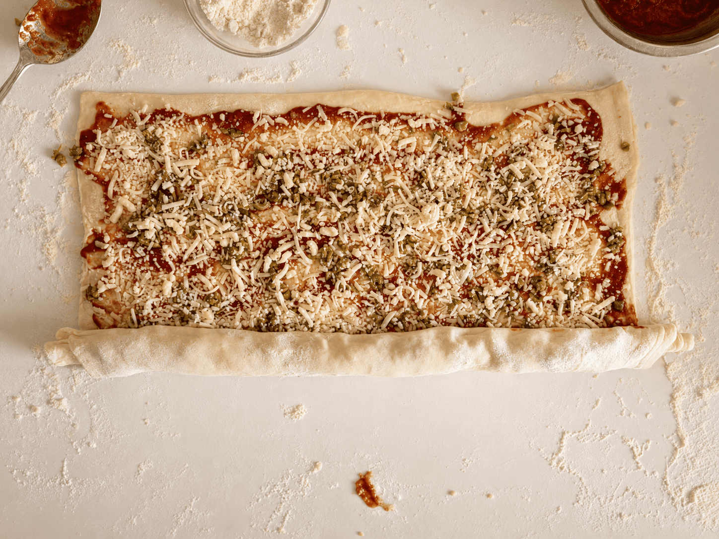 The topped puff pastry being rolled up from the long side into a log