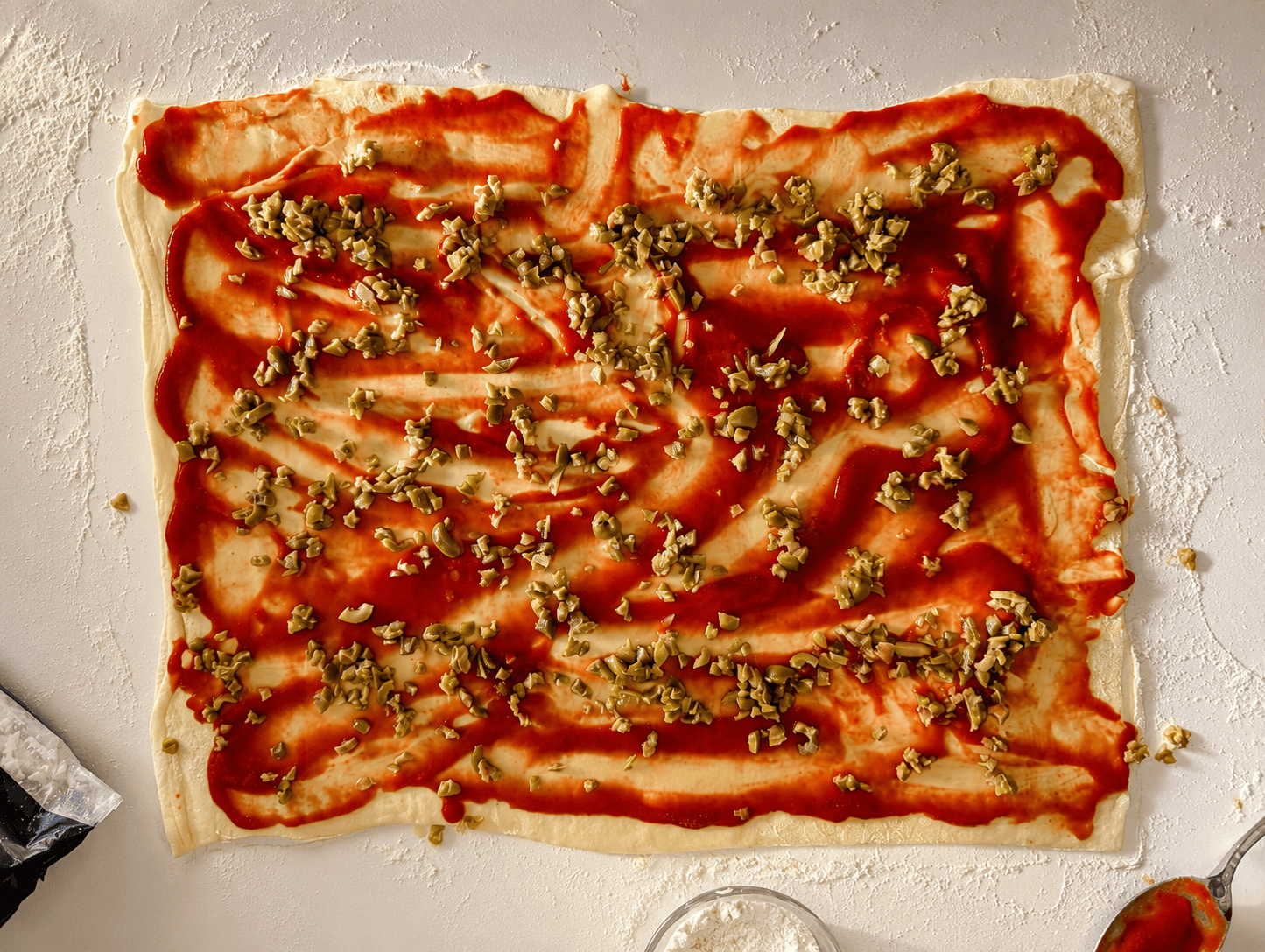 Puff pastry spread with tomato sauce and scattered with chopped green olives