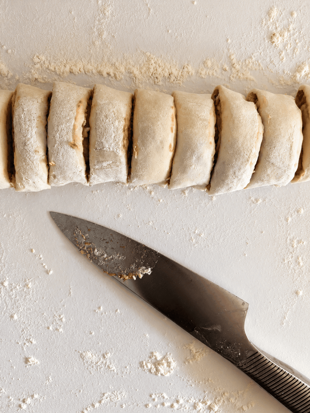 A rolled puff pastry log sliced into rounds next to a sharp knife