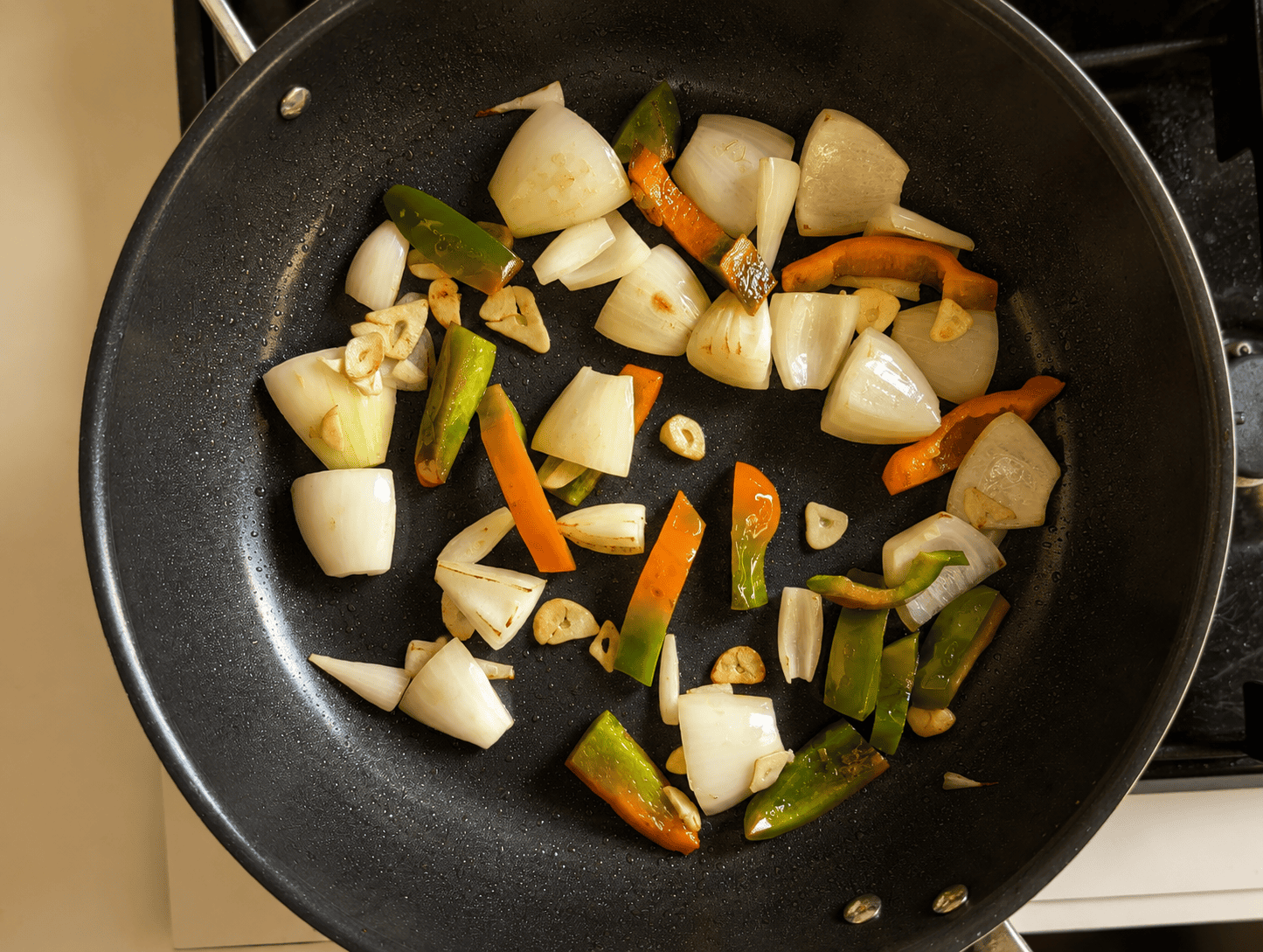Roughly chopped onion, garlic and bell pepper blistering in a hot pan for Thai green curry