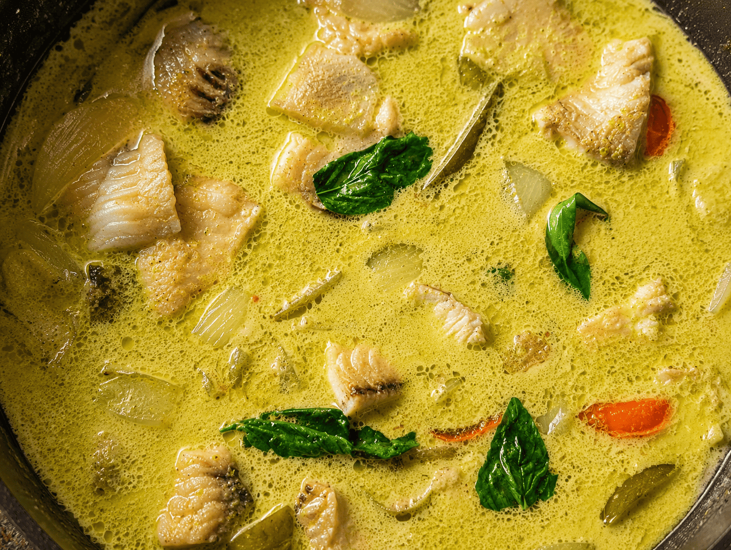 Close up of Thai green curry with chunks of white fish, basil leaves and red pepper in a creamy green sauce