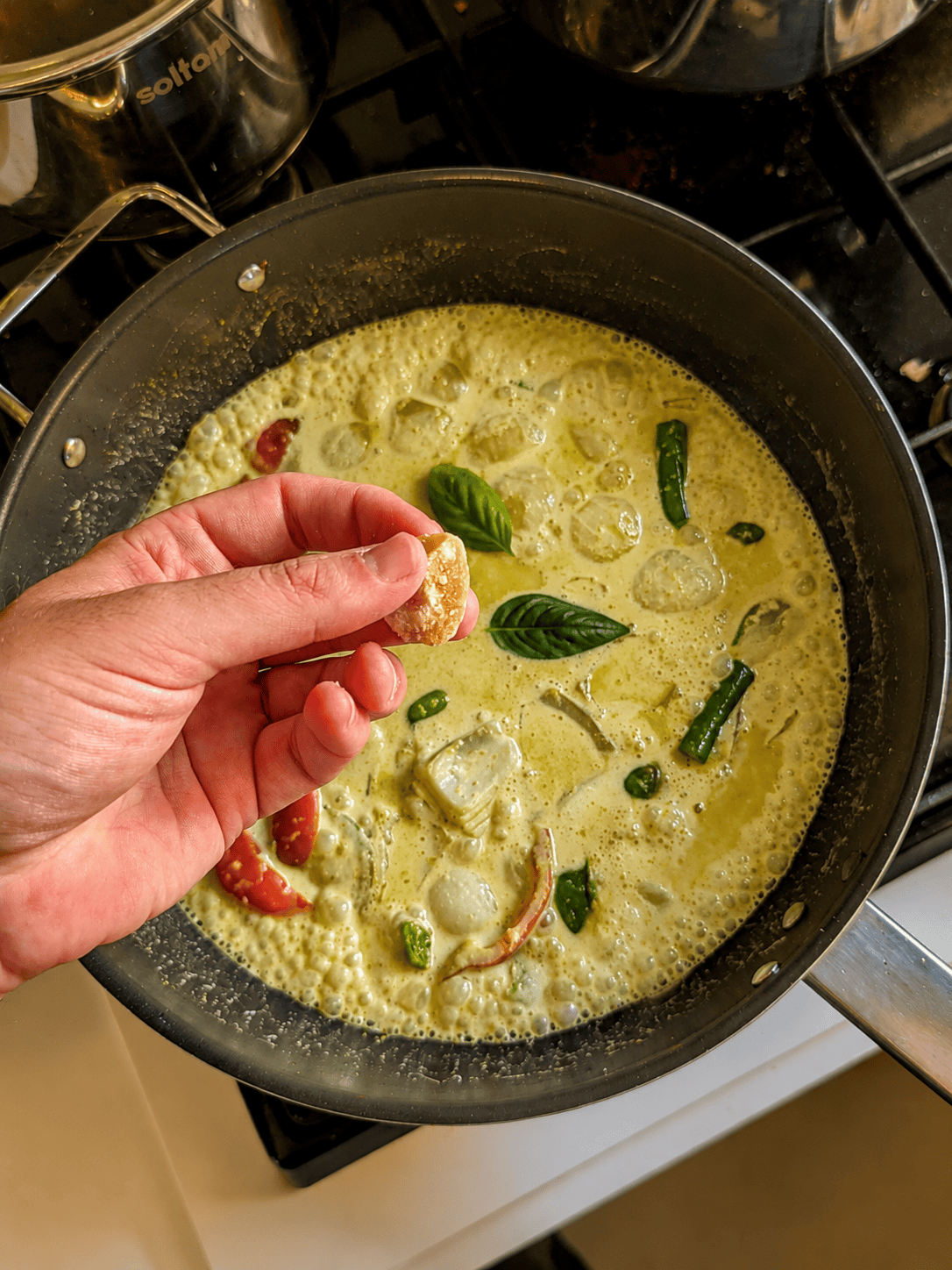 A piece of palm sugar being added by hand into a pan of Thai green curry