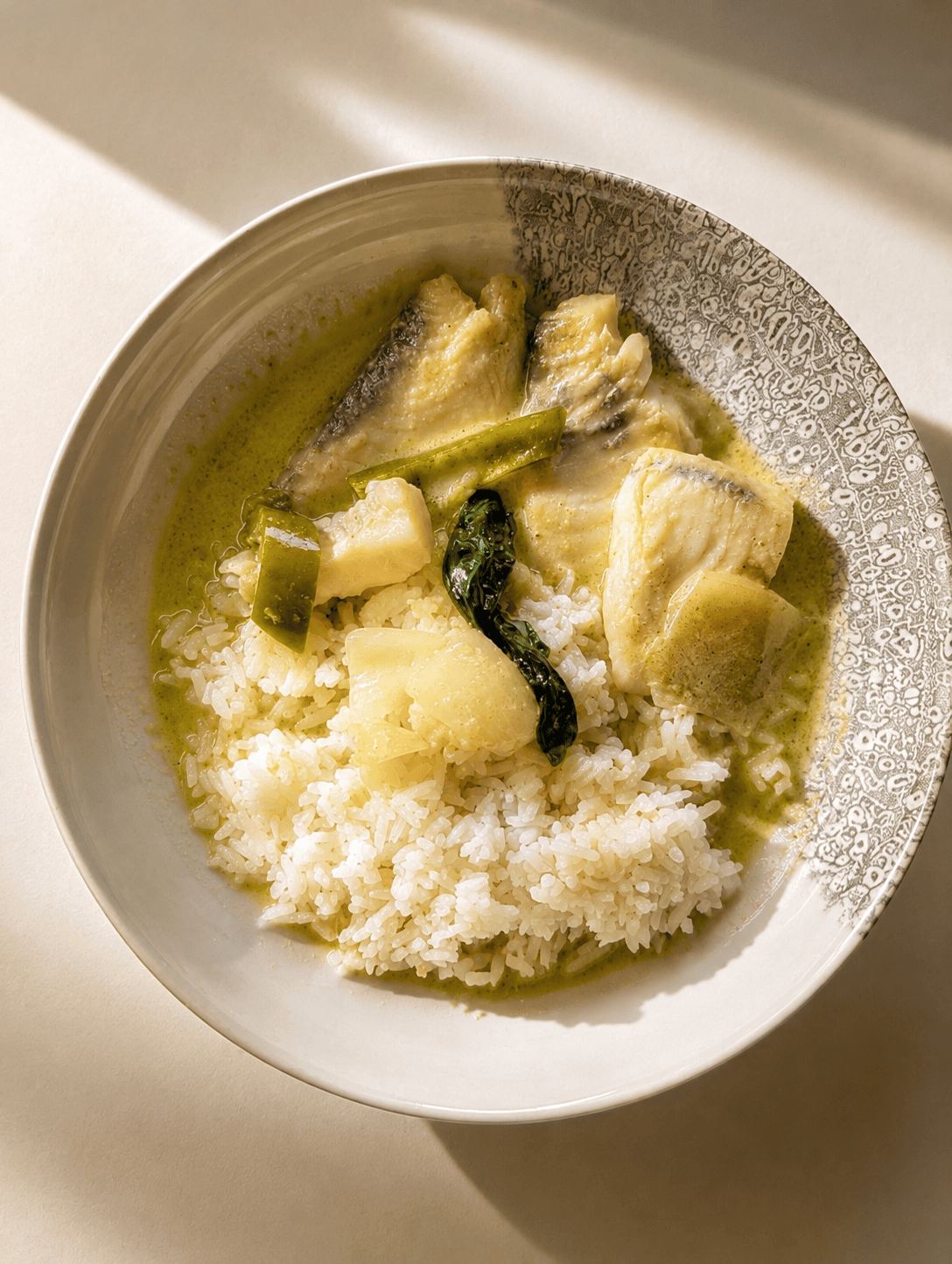 Thai green curry with fish served over white rice in a bowl with basil and green pepper