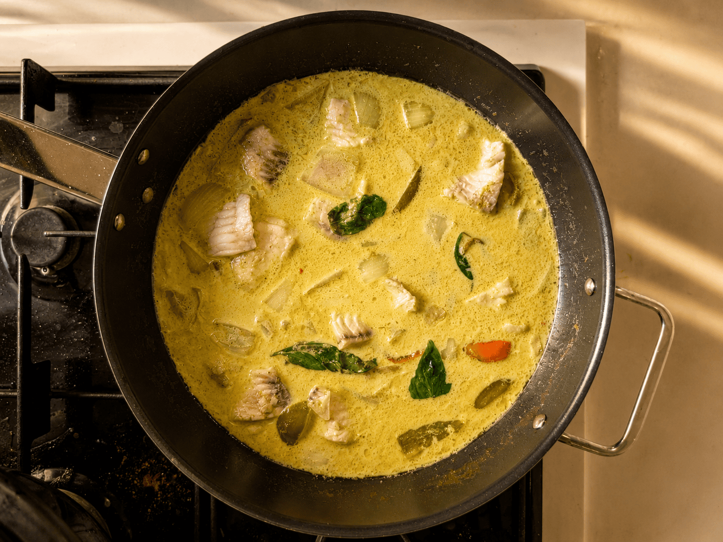 A pan of Thai green curry with fish and basil simmering gently on the stove