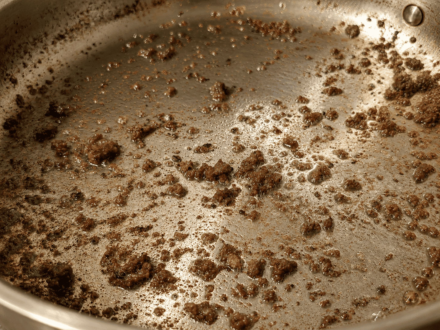 Empty stainless steel pan showing browned beef fond stuck to the bottom after the meat has been removed