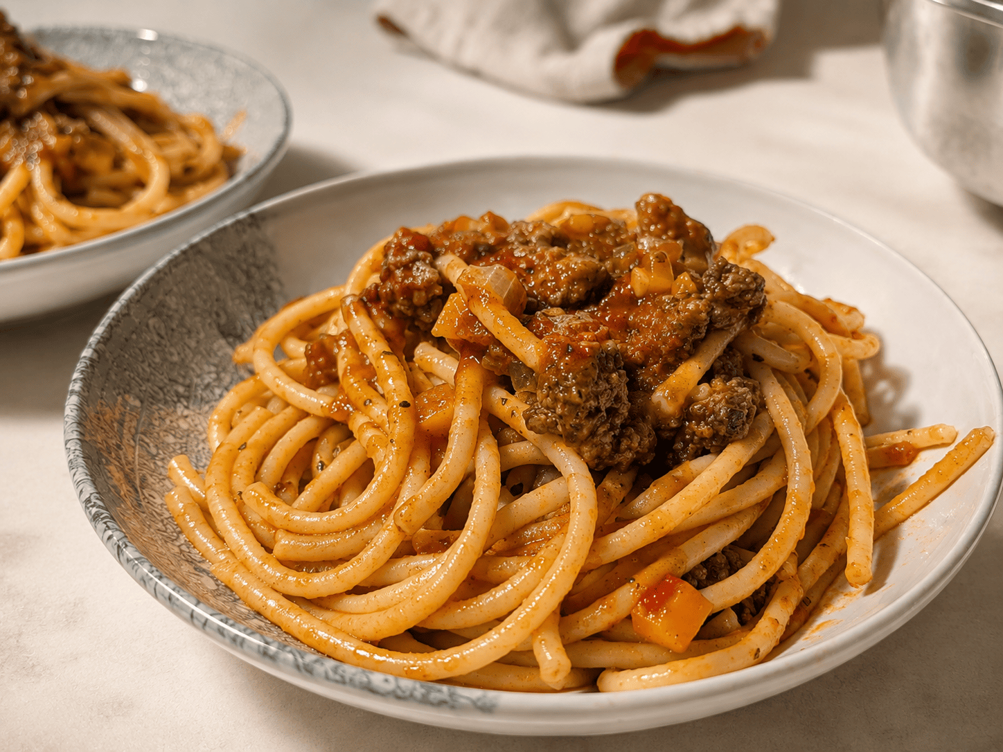 Two bowls of spaghetti topped with rich beef ragu sauce, close up on the front bowl with sauce clinging to the noodles