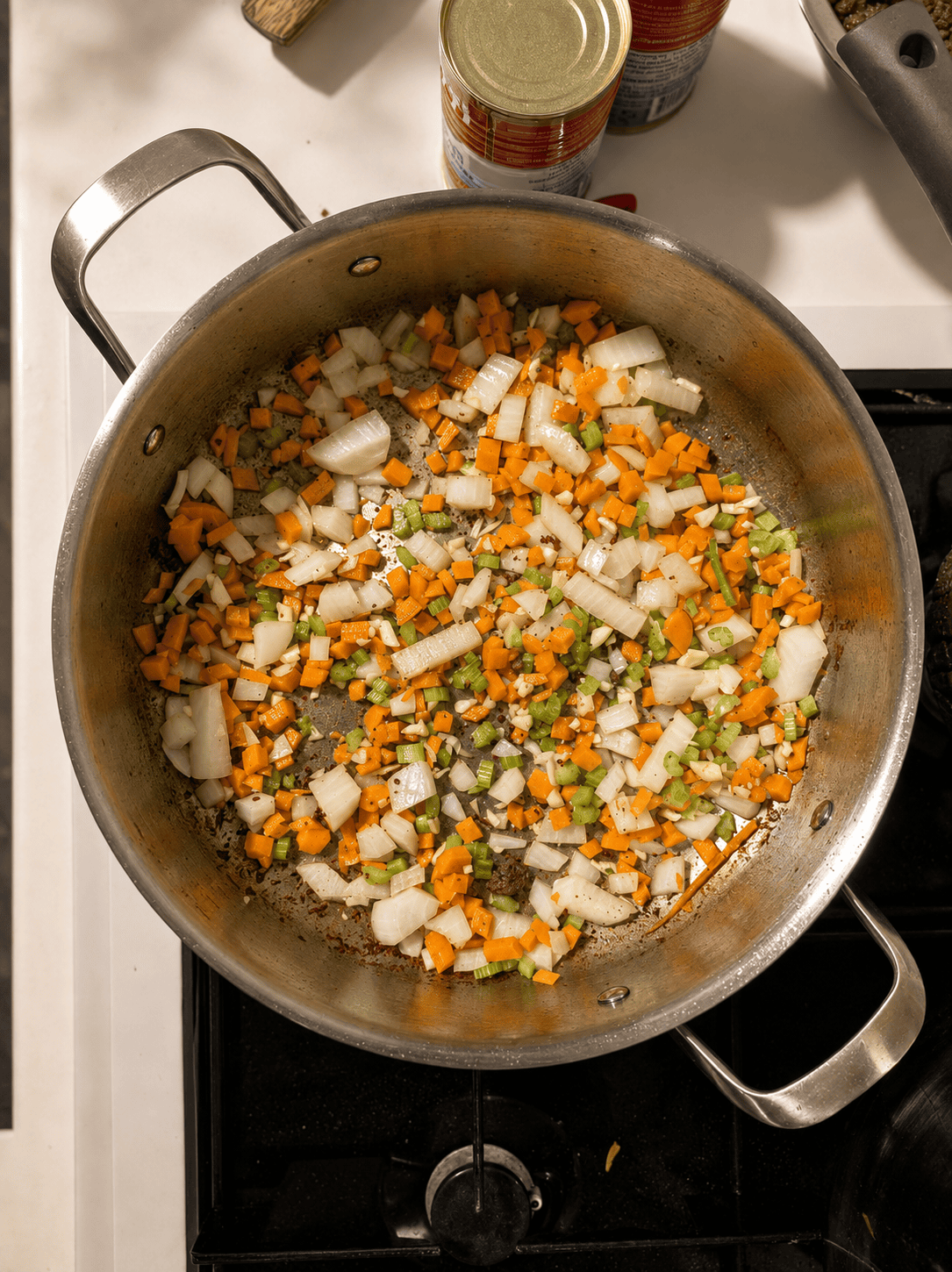 Diced onion, carrot, celery, and garlic sautéing in a stainless steel pan over the beef fond
