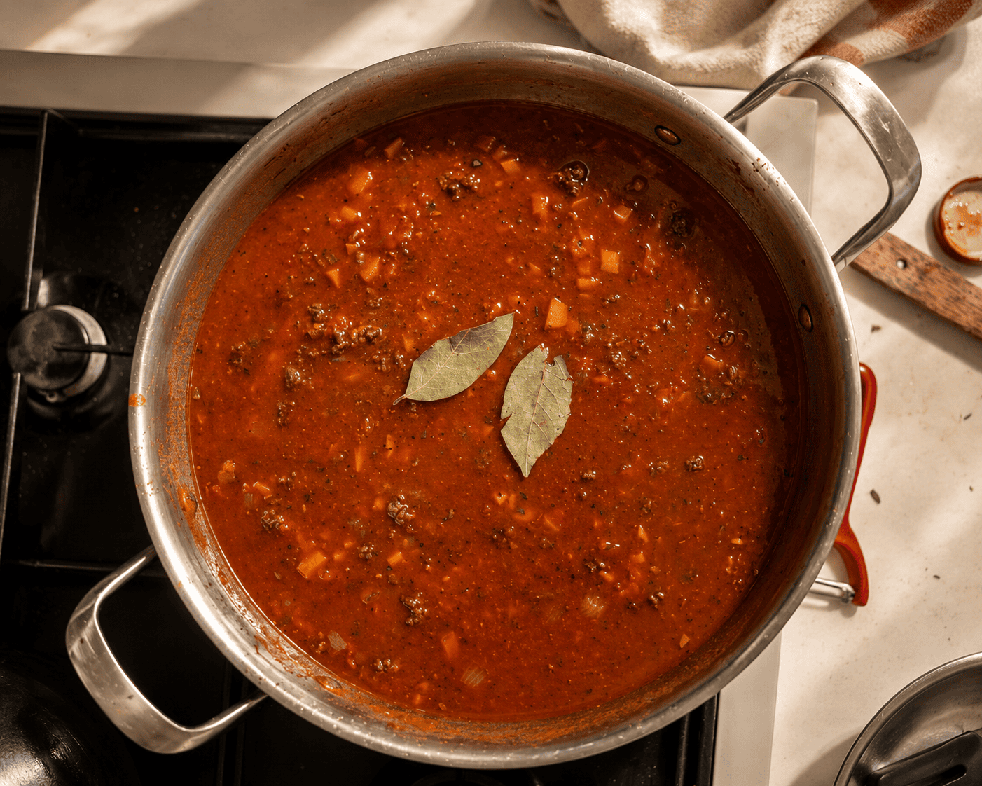 Beef ragu sauce simmering in a pan with two dried bay leaves floating on the surface