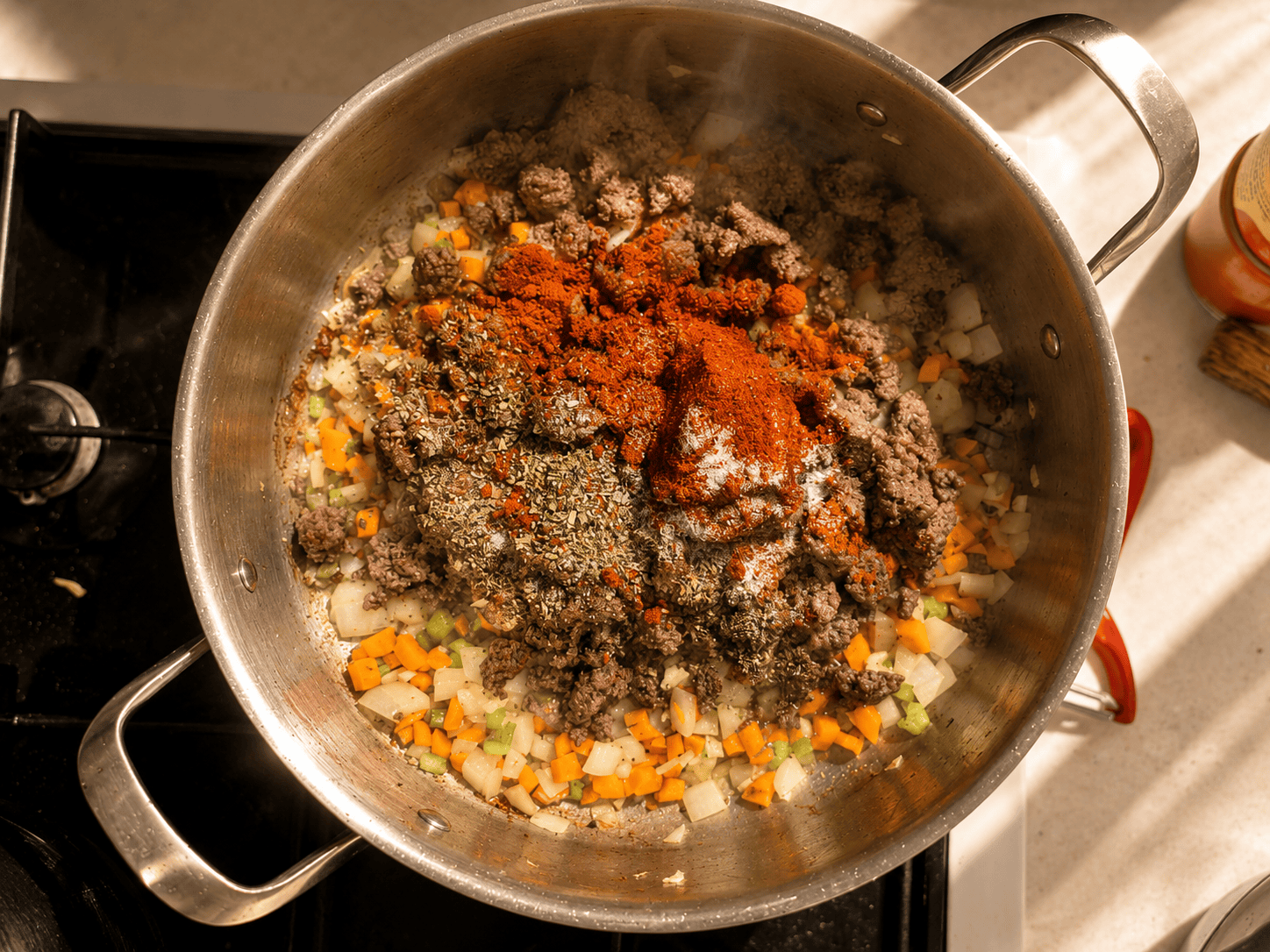 Paprika and dried oregano being added on top of browned ground beef and sautéed vegetables in a pan, with steam rising