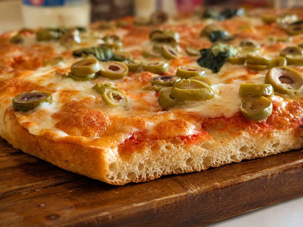 Close-up corner shot of the baked focaccia pizza showing melted cheese and lightly charred olive edges