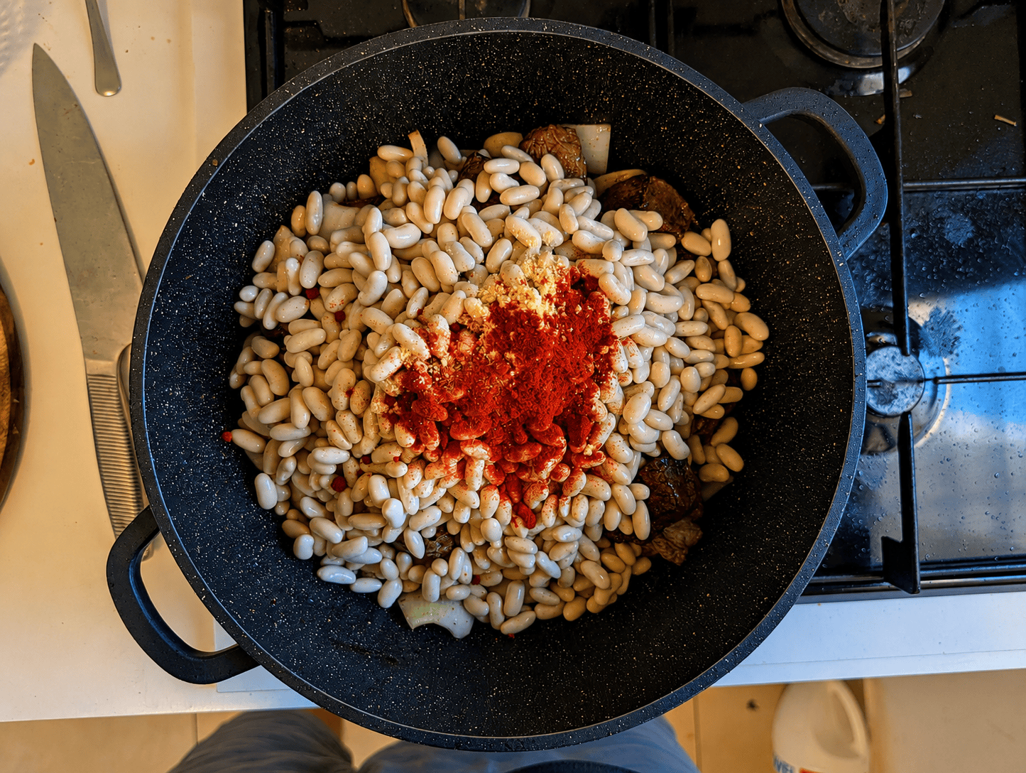 Soaked white beans in a pot with a pile of paprika and minced garlic sitting on top, not yet mixed in