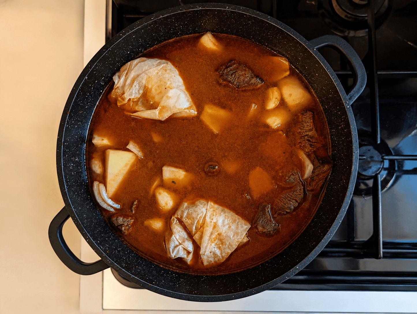 Two eggs wrapped in parchment paper sitting on top of the boiling beef and white bean stew, ready to be sealed and put in the oven