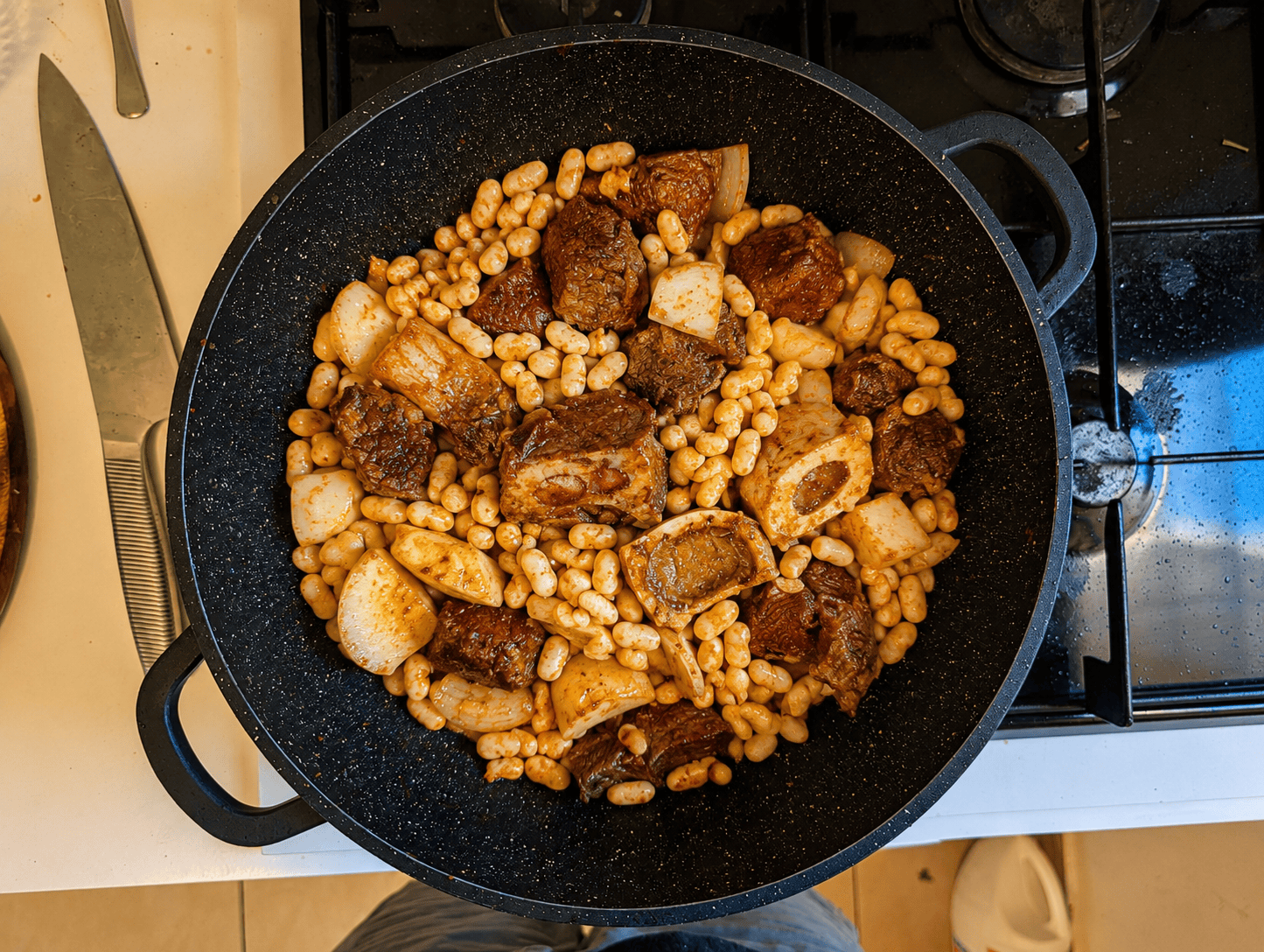 Beef, beans, potato, and onion mixed together in a pot, all coated in a deep reddish paprika color