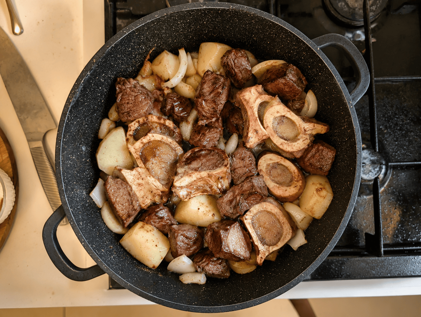 Beef cubes, marrow bones, potato cubes, and onion pieces frying together in a large pot