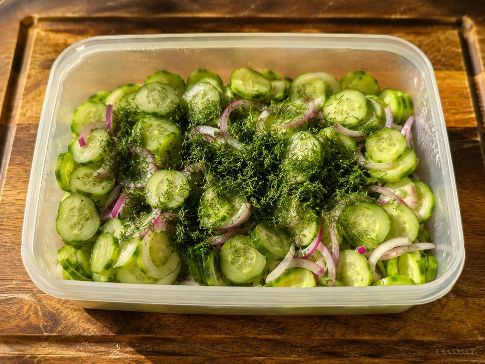 Sweet and sour cucumber salad in a container with fresh dill, ready to refrigerate