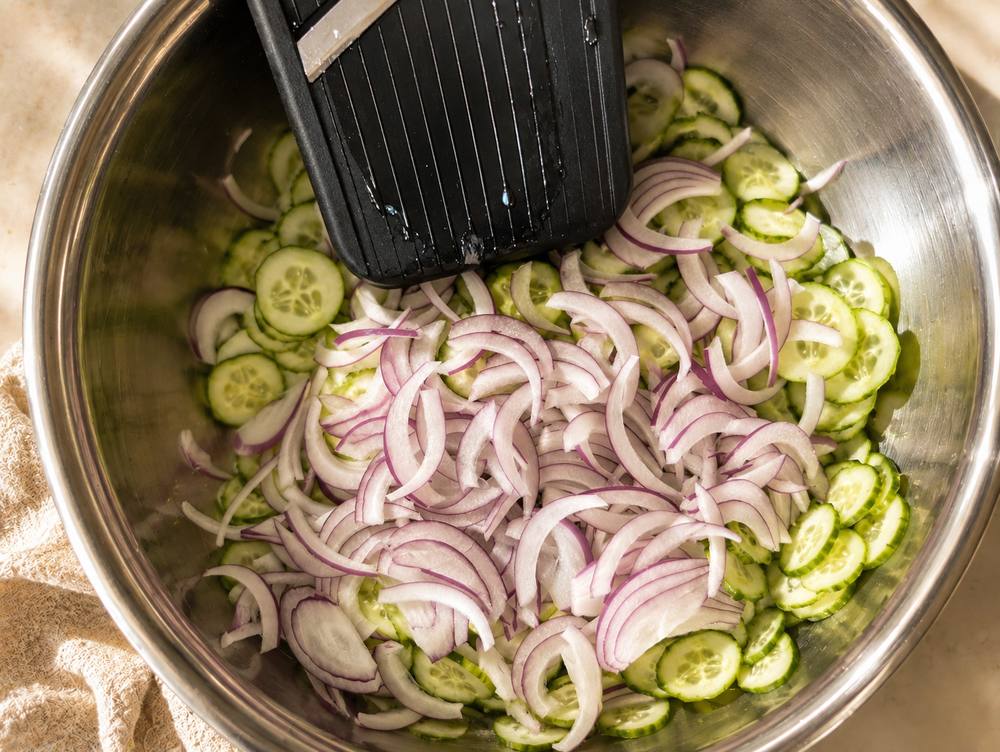 Cucumbers being sliced thin on a mandoline for sweet and sour cucumber salad