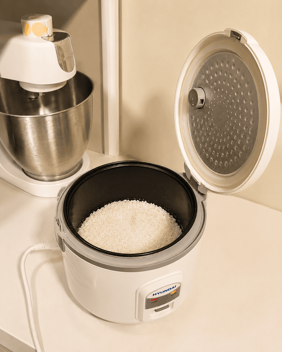 Soaked glutinous rice sitting in the bowl of a basic white rice cooker with the lid open, ready to cook