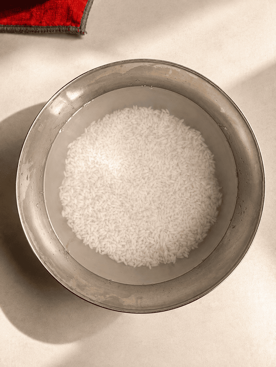 Glutinous rice soaking in cold water in a stainless steel bowl, grains settled in an even layer at the bottom