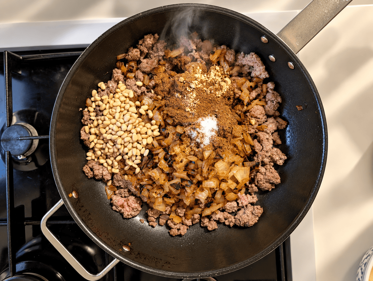 Baharat spice, salt, chicken powder and pine nuts added to browned ground beef and fried onions in a pan