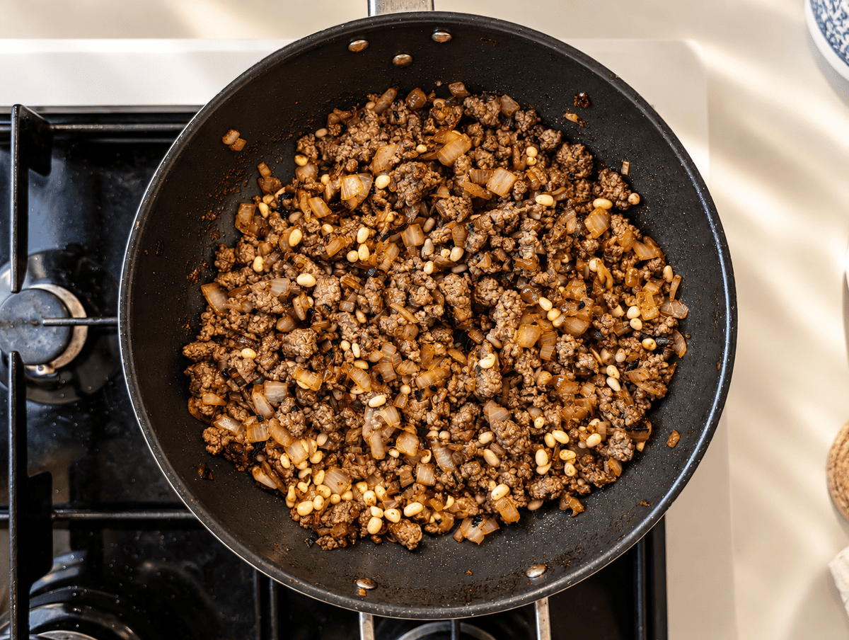 Finished kibbeh filling of spiced ground beef, golden fried onions and pine nuts in a black pan