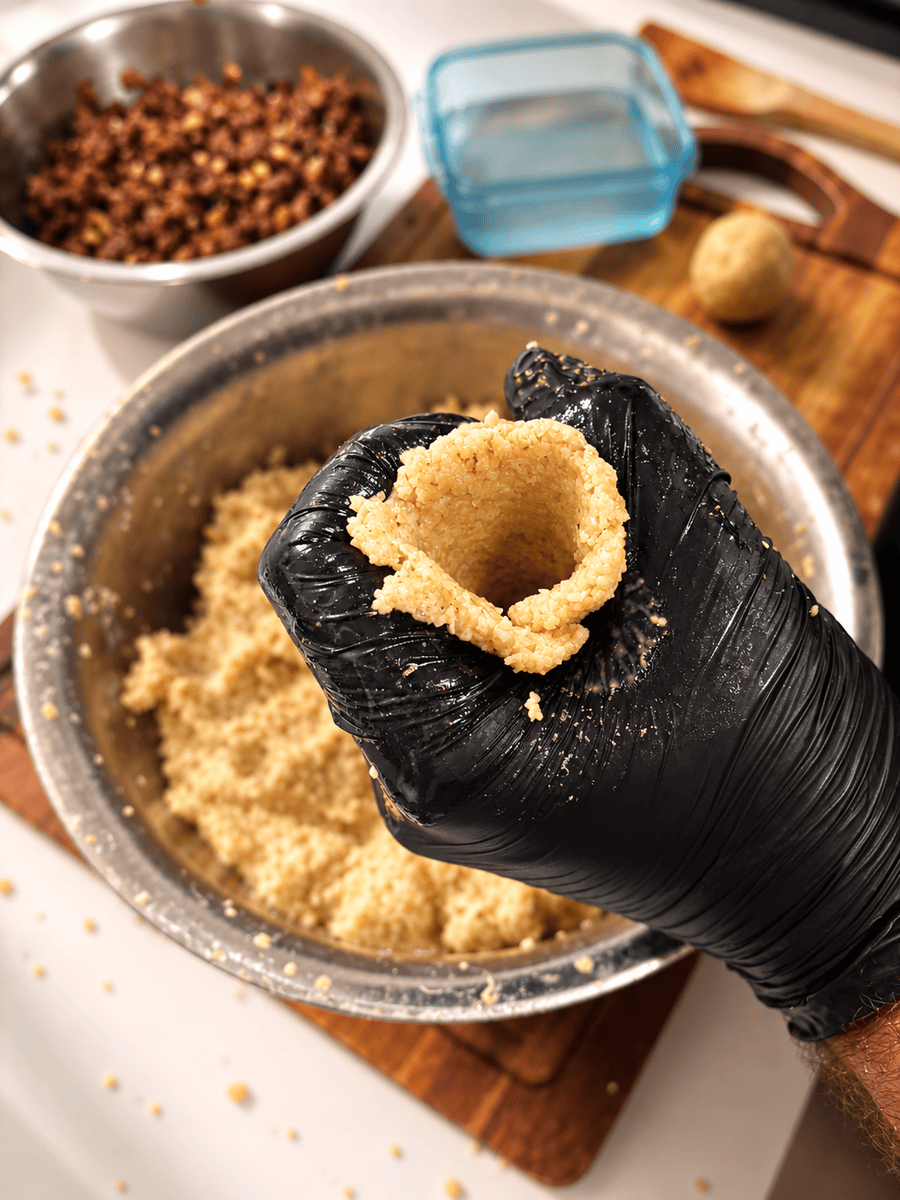 Gloved hand forming a hollow cup from bulgur kibbeh dough, walls thinned and ready for filling