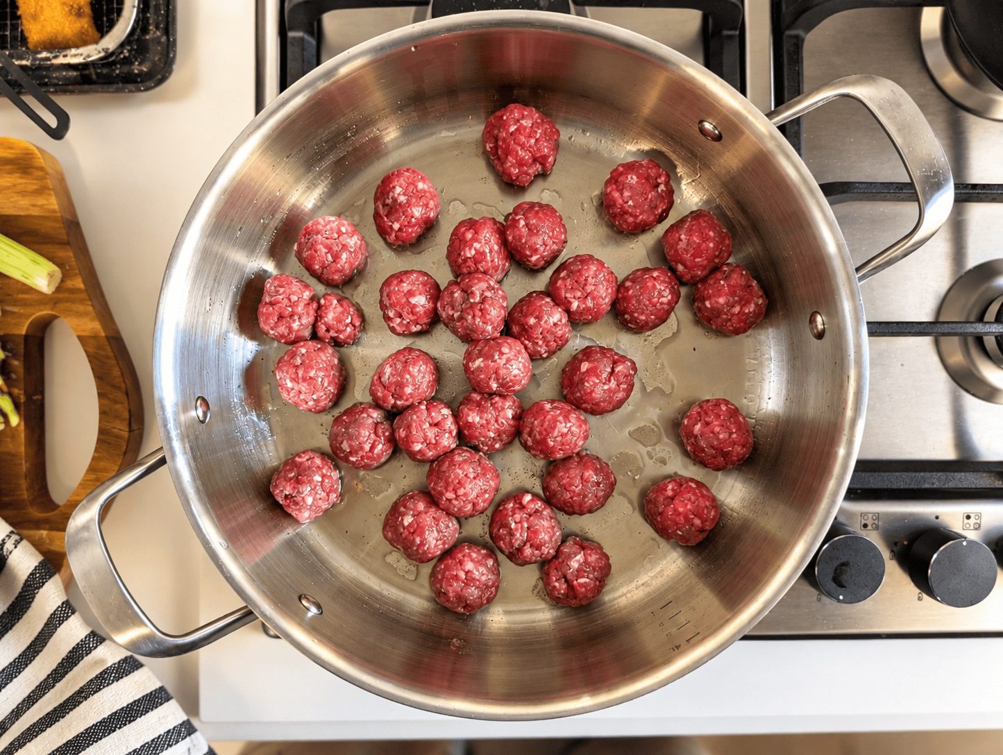 Raw ground beef meatballs arranged in a wide stainless steel pan, ready to be browned