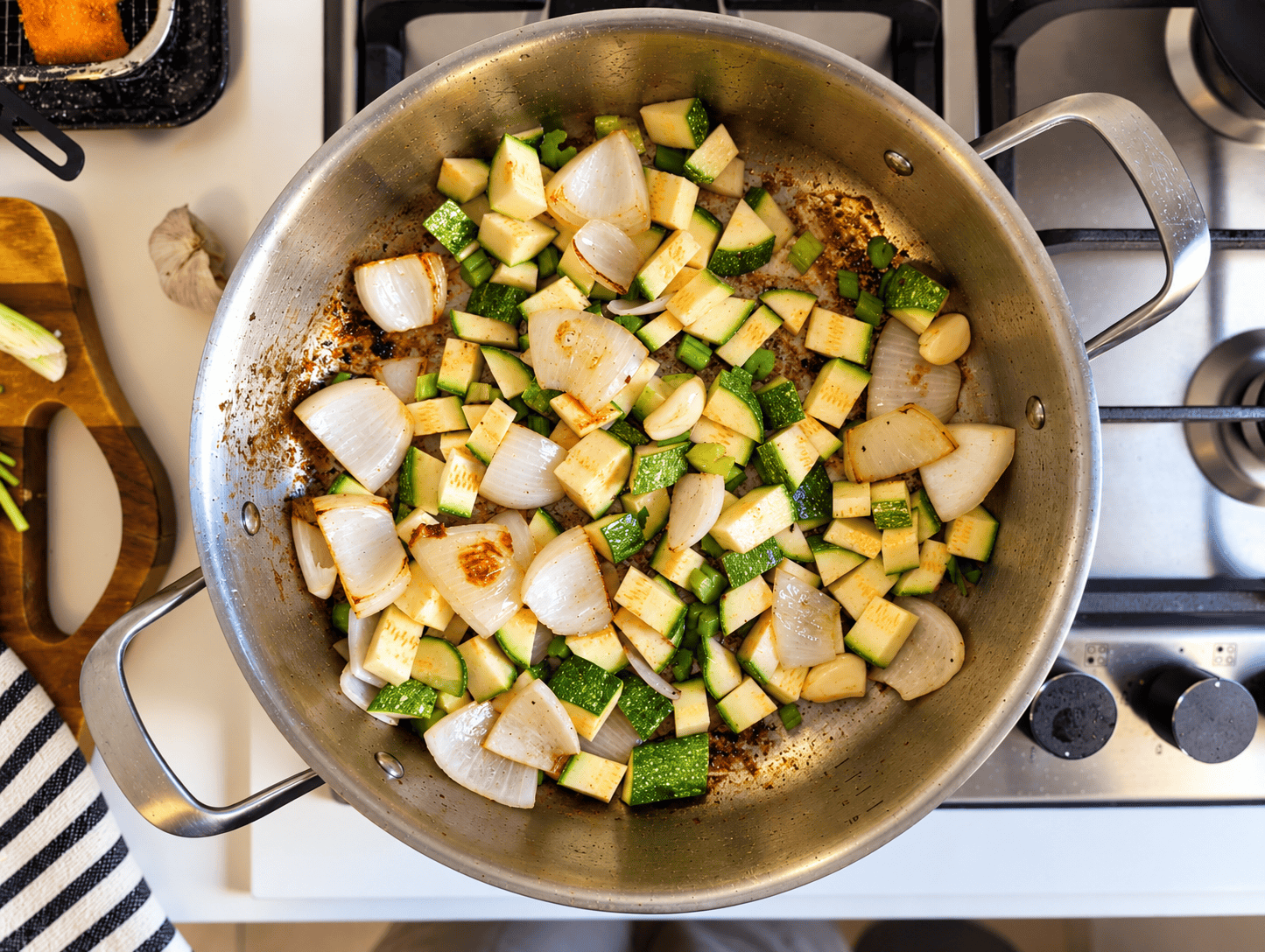 Chopped zucchini, onion and celery sauteing in a stainless steel pan on the stovetop